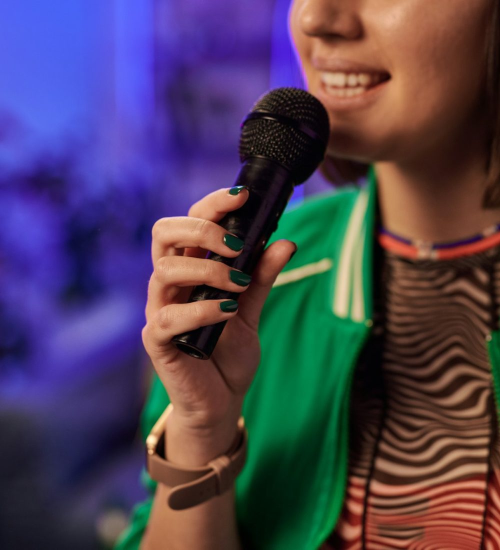 Young brunette woman in green jacket performing karaoke song